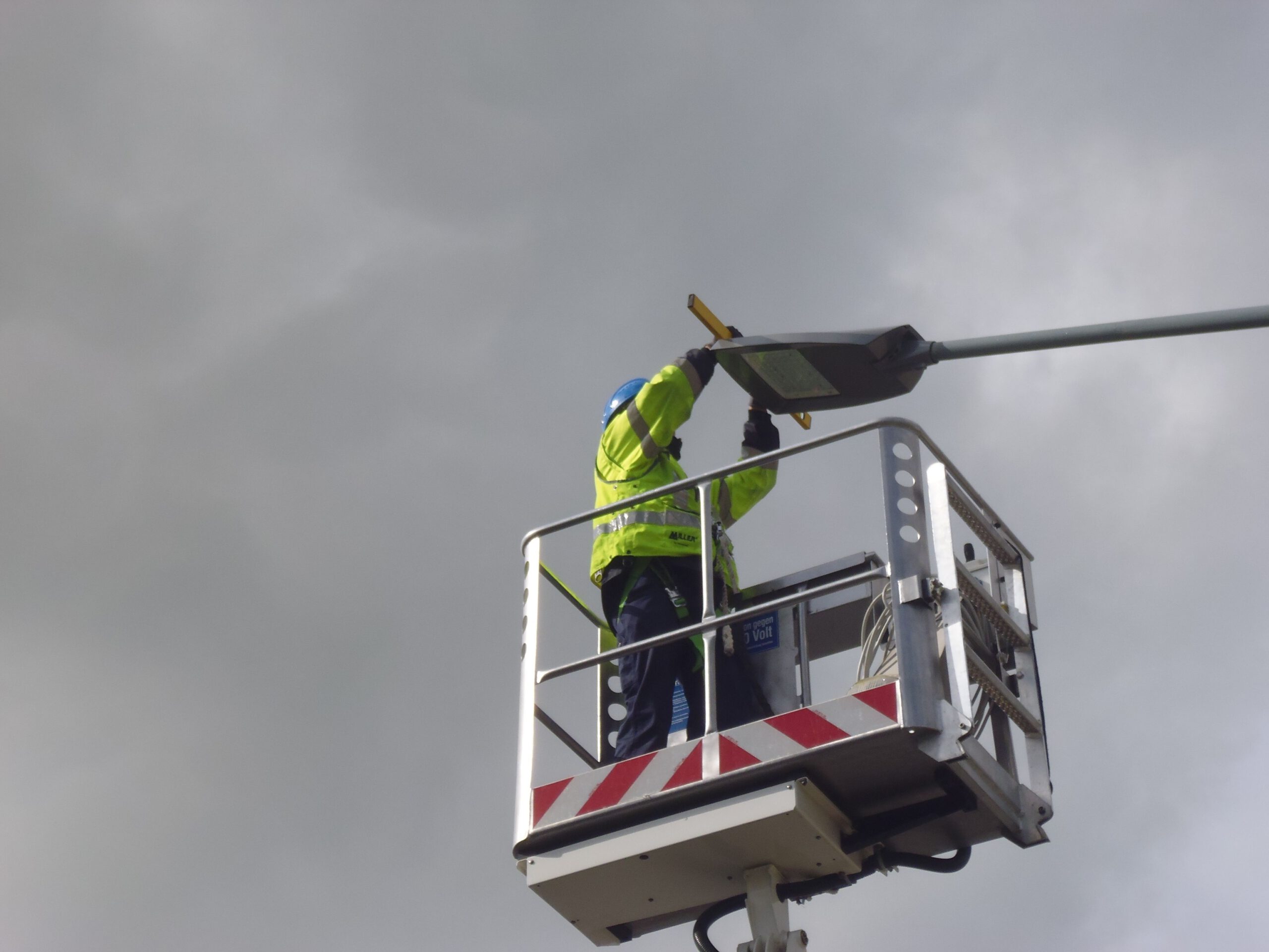 FBG-Elektroniker in Arbeitskleidung mit Schutzhelm arbeitet auf einer Hebebühne an einer Straßenlaterne im Fischereihafen.