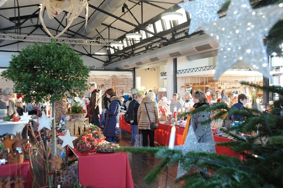 Kunsthandwerkermarkt im Fischbahnhof: Besuchende stöbern an roten Tischen, Tanne am rechten Bildrand.