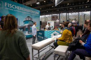 Auf einer Messe hält ein Mann an einem Stand einen Vortrag.